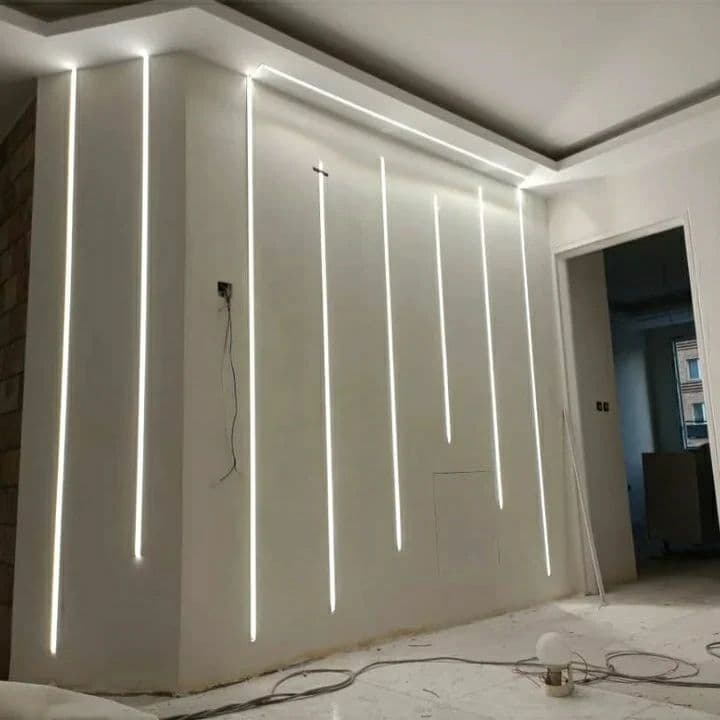 Modern white wall featuring vertical recessed LED light strips of varying lengths in a minimalist room.