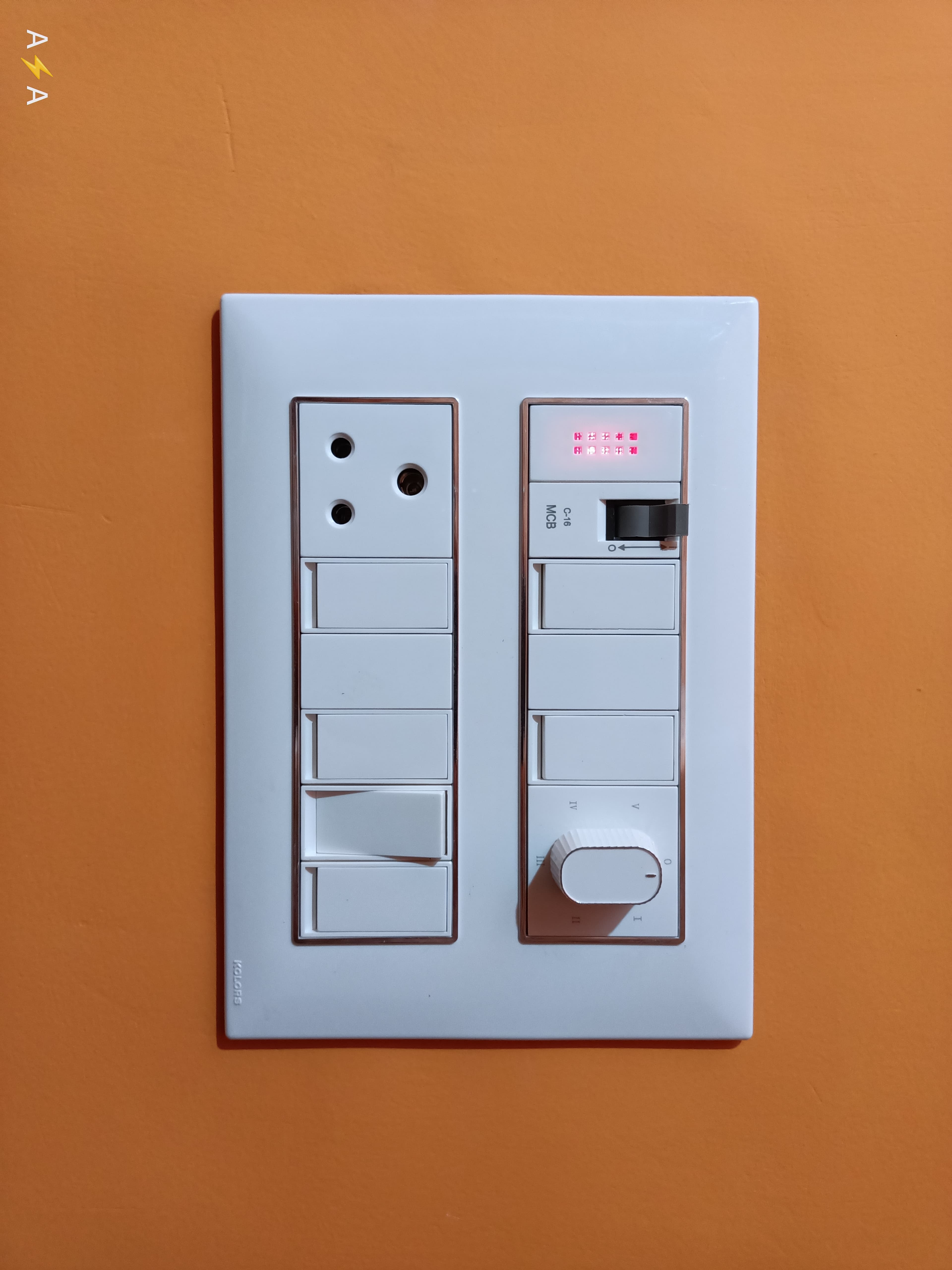 White electrical switchboard with socket, switches, and fan regulator on a bright orange wall.