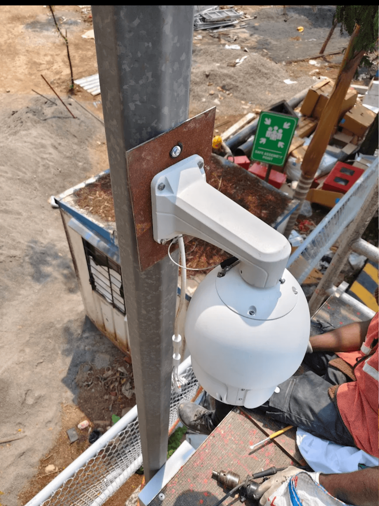 White dome security camera mounted on a metal pole overlooking a construction site.